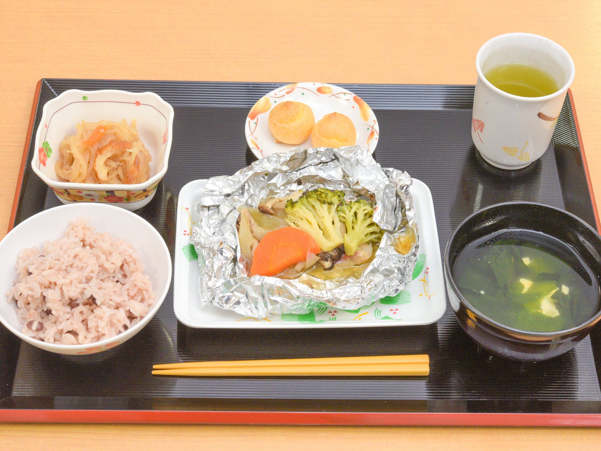 メインディッシュはブロッコリーとニンジンのホイル焼きで、四角い皿に盛られている。主食は赤飯で、デザート付き。