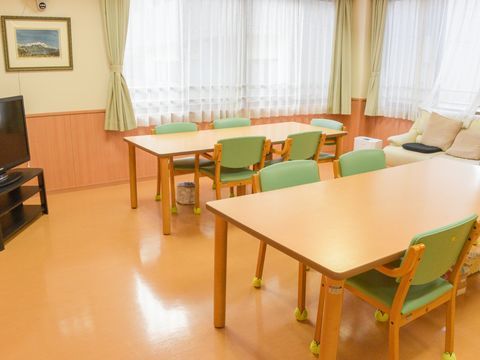 2面がガラス窓になっており、採光が十分で明るいリビング。食卓が2セットのほか、テレビとソファーが置かれている。