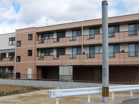ブロック塀と黒色のフェンスで囲まれた敷地に建っている３階建ての施設外観