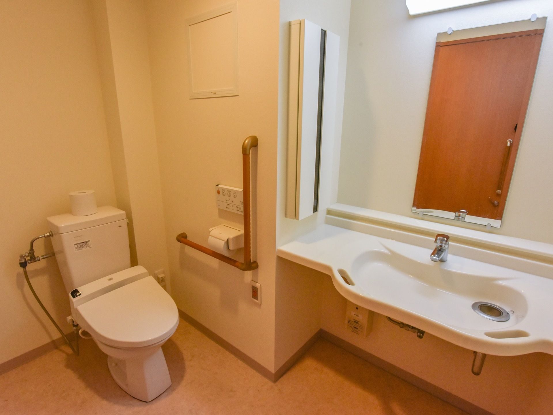 温水洗浄機能付きの洋式トイレである。入口の目の前には、鏡と照明が付いた横幅のある洗面台が設置されている。