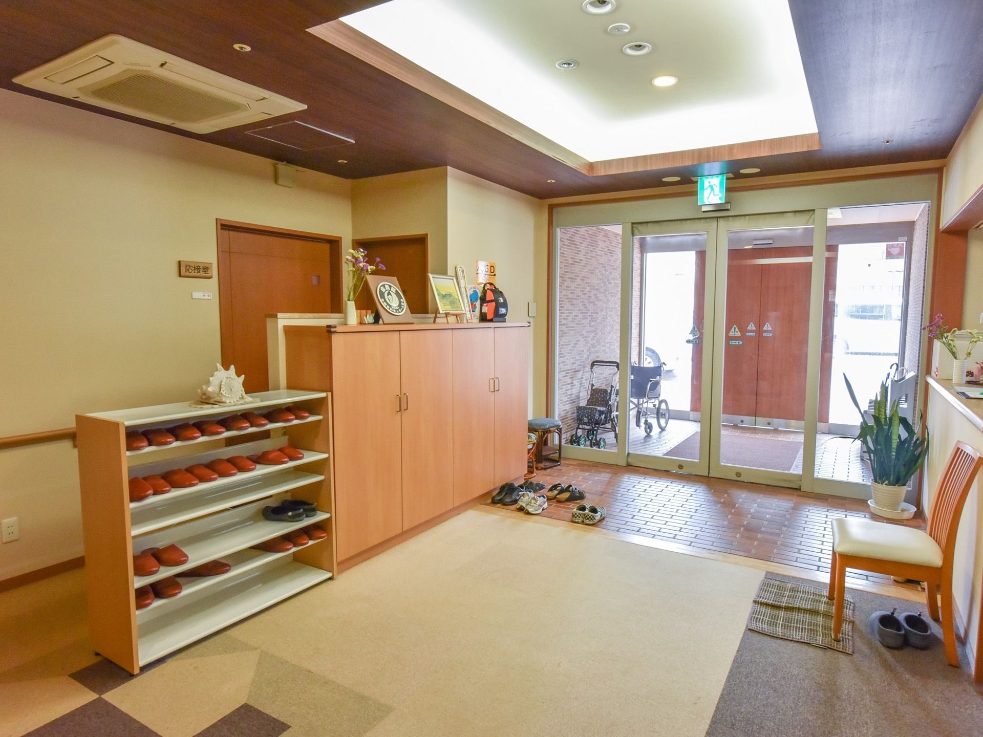 木製の扉が付いた靴箱の横に、スリッパがたくさん収納された棚が設置されている。玄関の奥には応接室が見える。