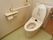 壁に手すりが設置されている。暖房便座付きトイレである。床はパステルグリーン、壁は白色の配色で明るい雰囲気である。