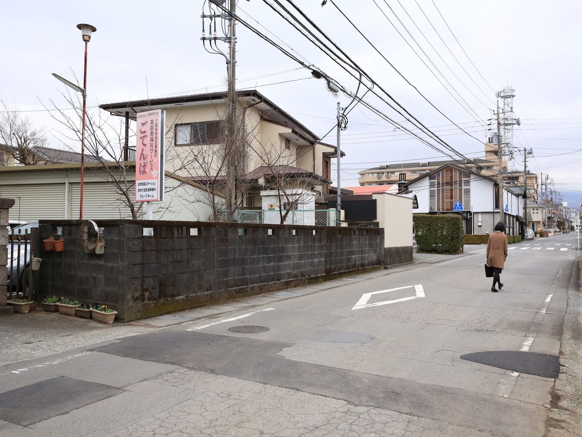 道路から見える場所に、ピンクを基調とした縦長の看板が設置されている。塀にはカーブミラーを設置している。