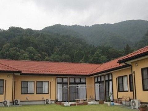 すぐ後ろに山並みがある、赤色の屋根とオレンジ色の外壁が特徴的な施設外観