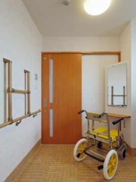 正面に扉があり、床はクッションフロアが貼られている。壁は白く、向かって右側には床と平行に長く、その上にＨ字型を倒した形に手すりが付いている。