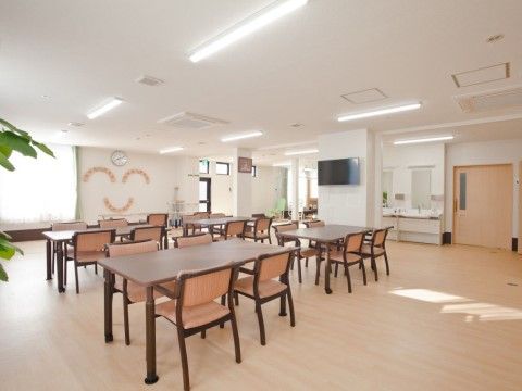 壁掛けテレビと洗面台があり、中央にテーブルと椅子が並べられた食堂