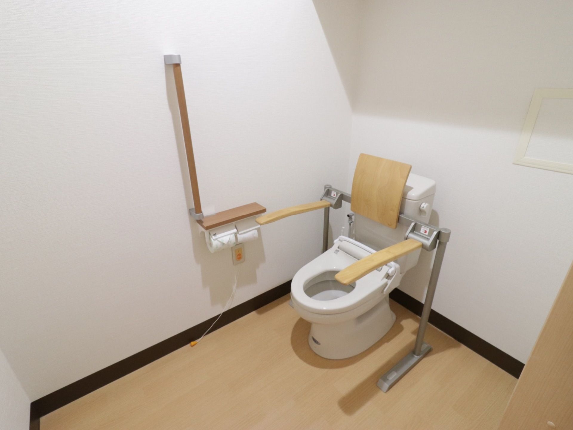 補助用の手すりの他に肘掛と背もたれが備わっているトイレである。全体的にすっきりとしたデザインでまとめられている。