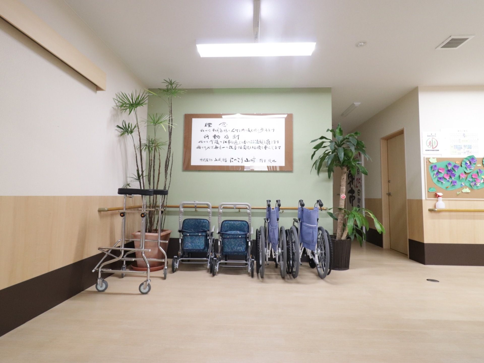 フローリングで段差のない廊下がある。壁には手すりがついている。入居者様が制作した作品が飾られている。