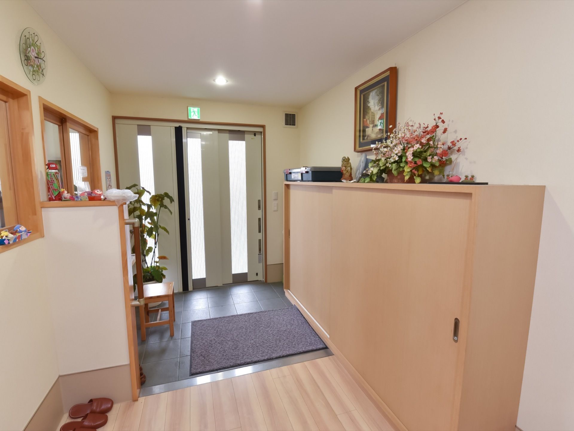 建物の内側から見た施設の玄関口。ドアが３段スライド式になっており、その上部には非常口誘導灯が灯っている。