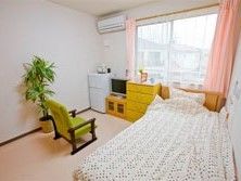 椅子やベッド、冷蔵庫、エアコンがある施設内の居室の様子。窓の外から景色が眺められる