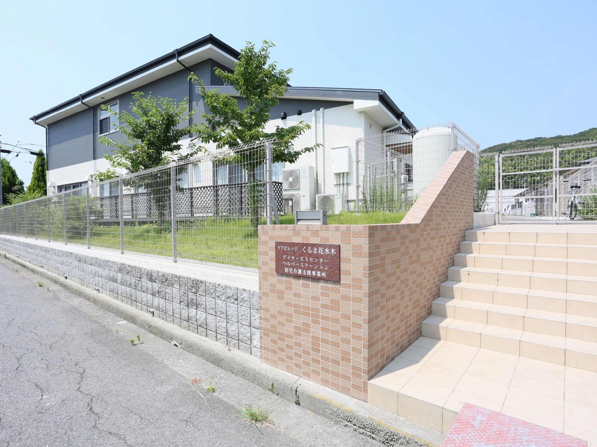 道路から階段を登ったところにある施設である。塀に施設名の書かれた看板が取りつけられており、上は芝生になっている。