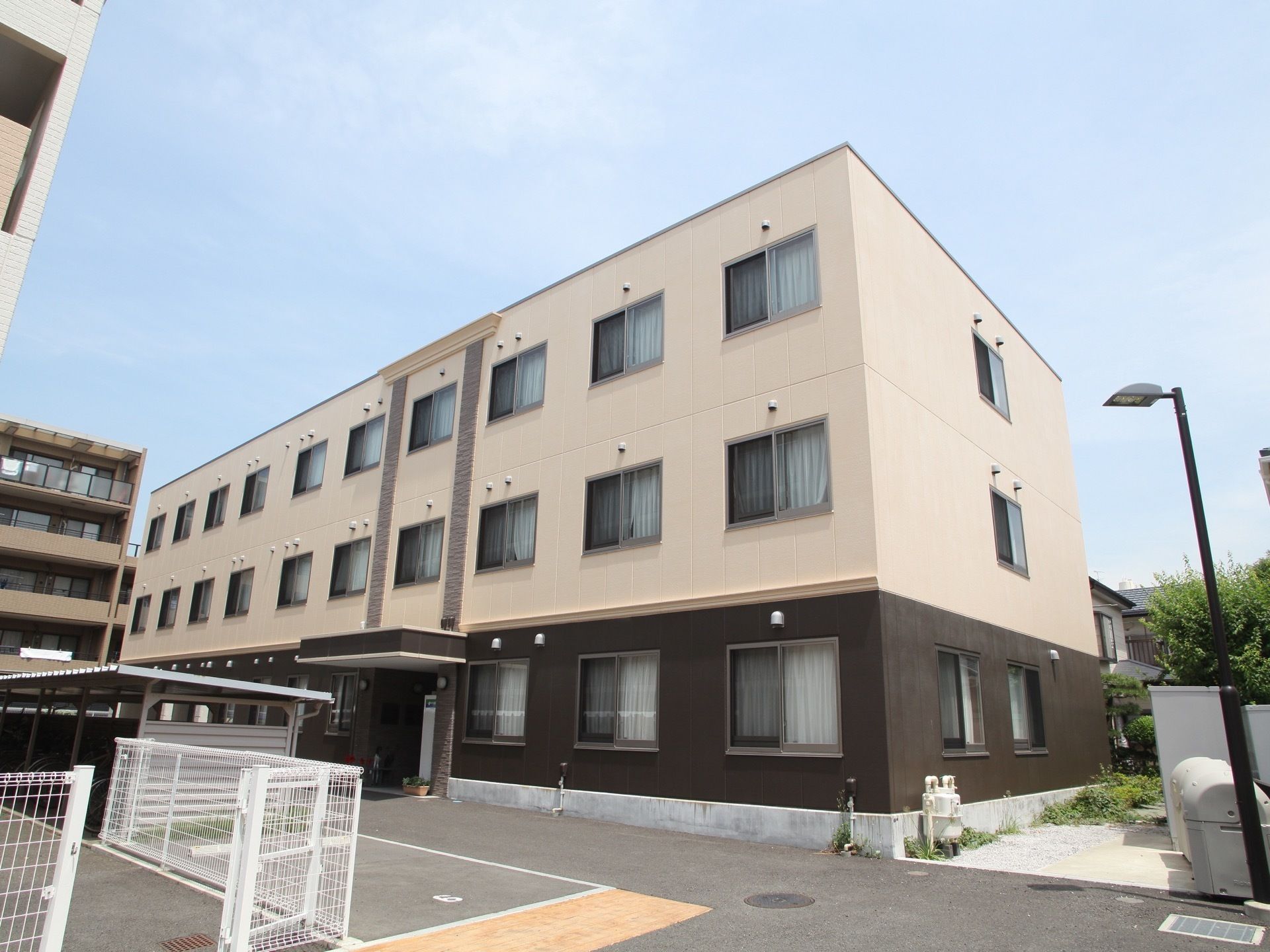 3階建ての建物で、1階部分は茶色で、2階以上はベージュの外壁になっている。玄関の上には屋根があり、車が近くまで入れるようになっている。
