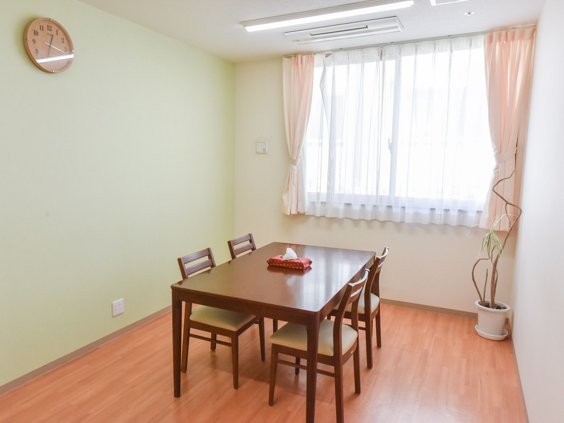 フローリングの部屋に茶色いテーブルと椅子が設置されている。テーブルの上にはティッシュペーパーの箱が一つ置いてある。