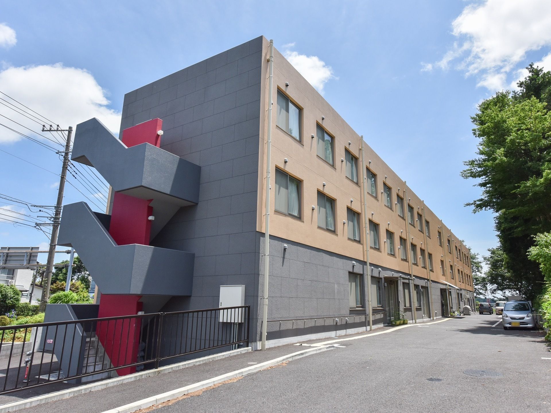 なだらかな坂を登ったところに施設の建物がある。グレーをベースとした色の３階建てで、外階段がついている。駐車スペースもある。