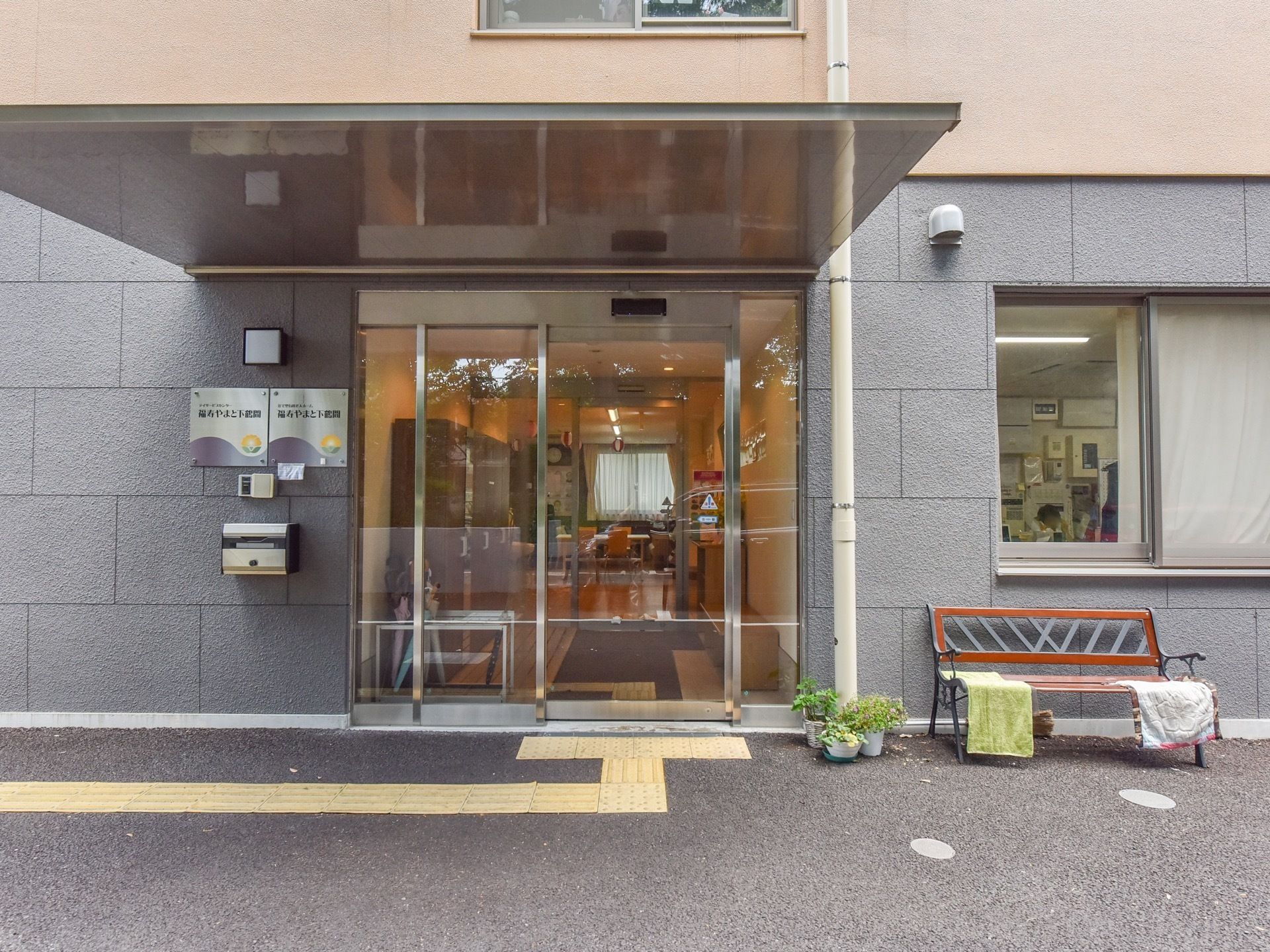 入口の上には小さな屋根がついている。横の壁には施設名と施設の種類を表示したプレートが掲げられている。郵便ポストも設置されている。