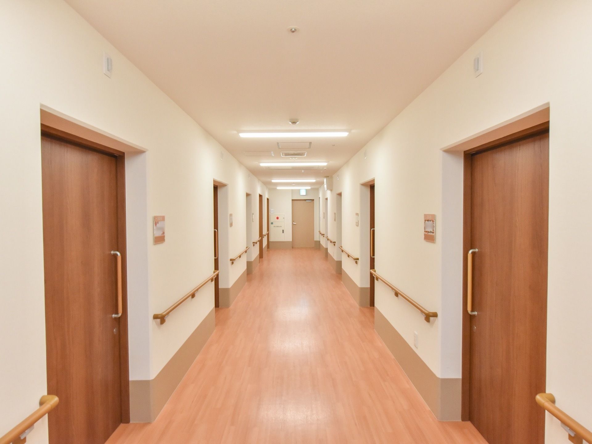施設内の廊下は横幅があり、床は全面フローリングになっている。両サイドには、入居者様の居室がたくさん並んでいる。