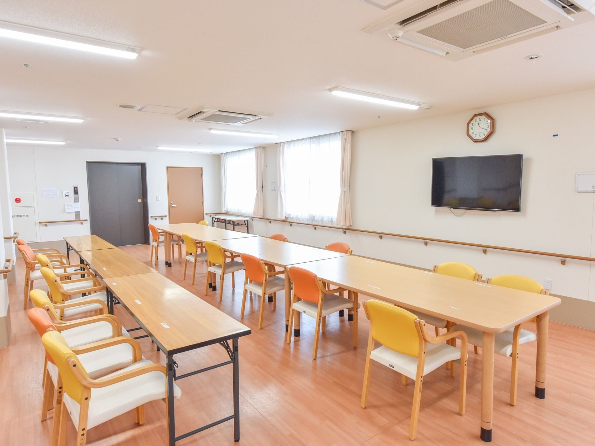 ゆったりとした広さの食堂には、長テーブルと椅子がたくさん並べられている。壁には、テレビと時計が掛けられている。