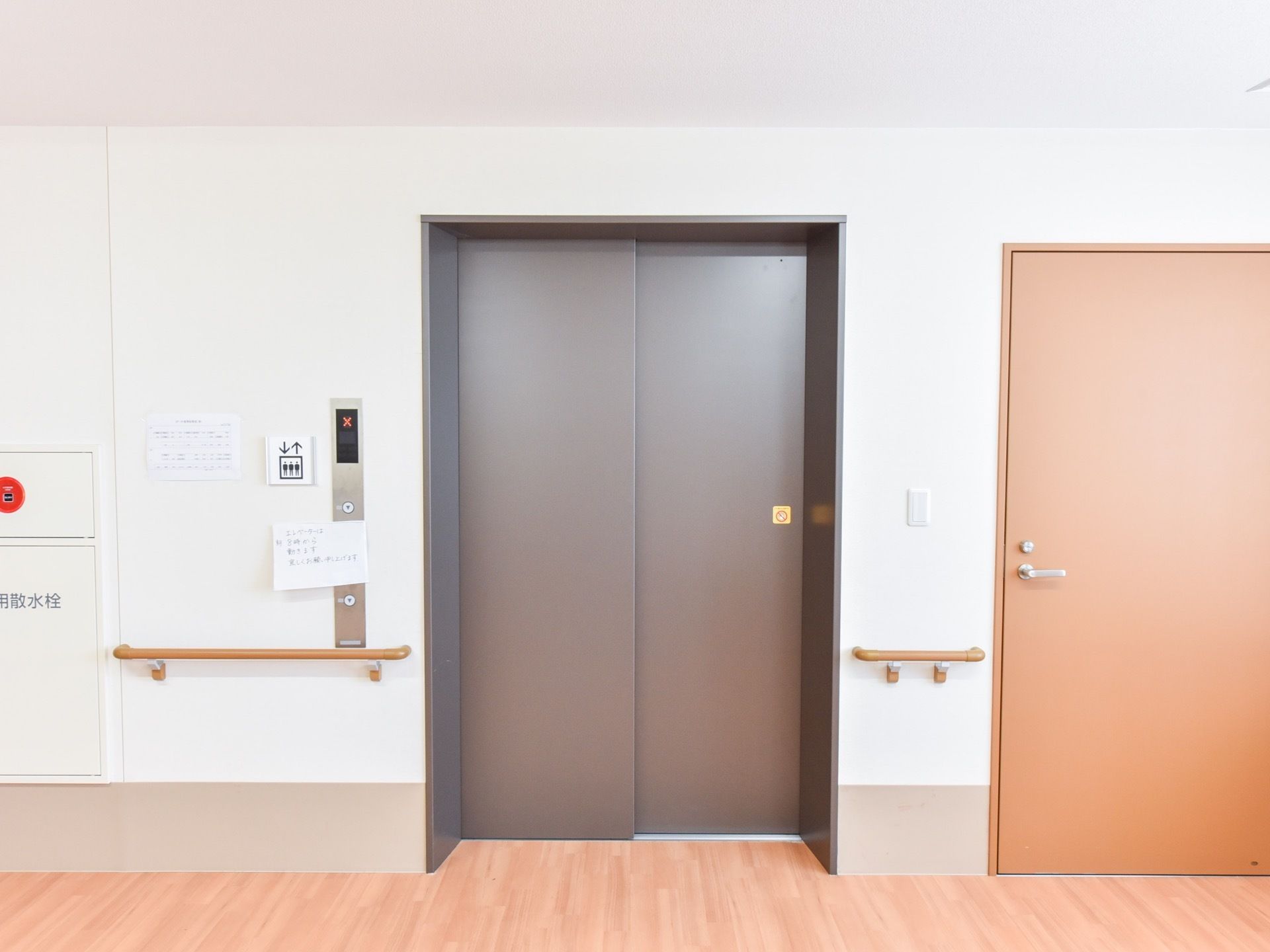 施設内には、黒い扉のエレベーターが設置されている。壁には、腰の高さの部分に茶色い手すりが取りつけられている。
