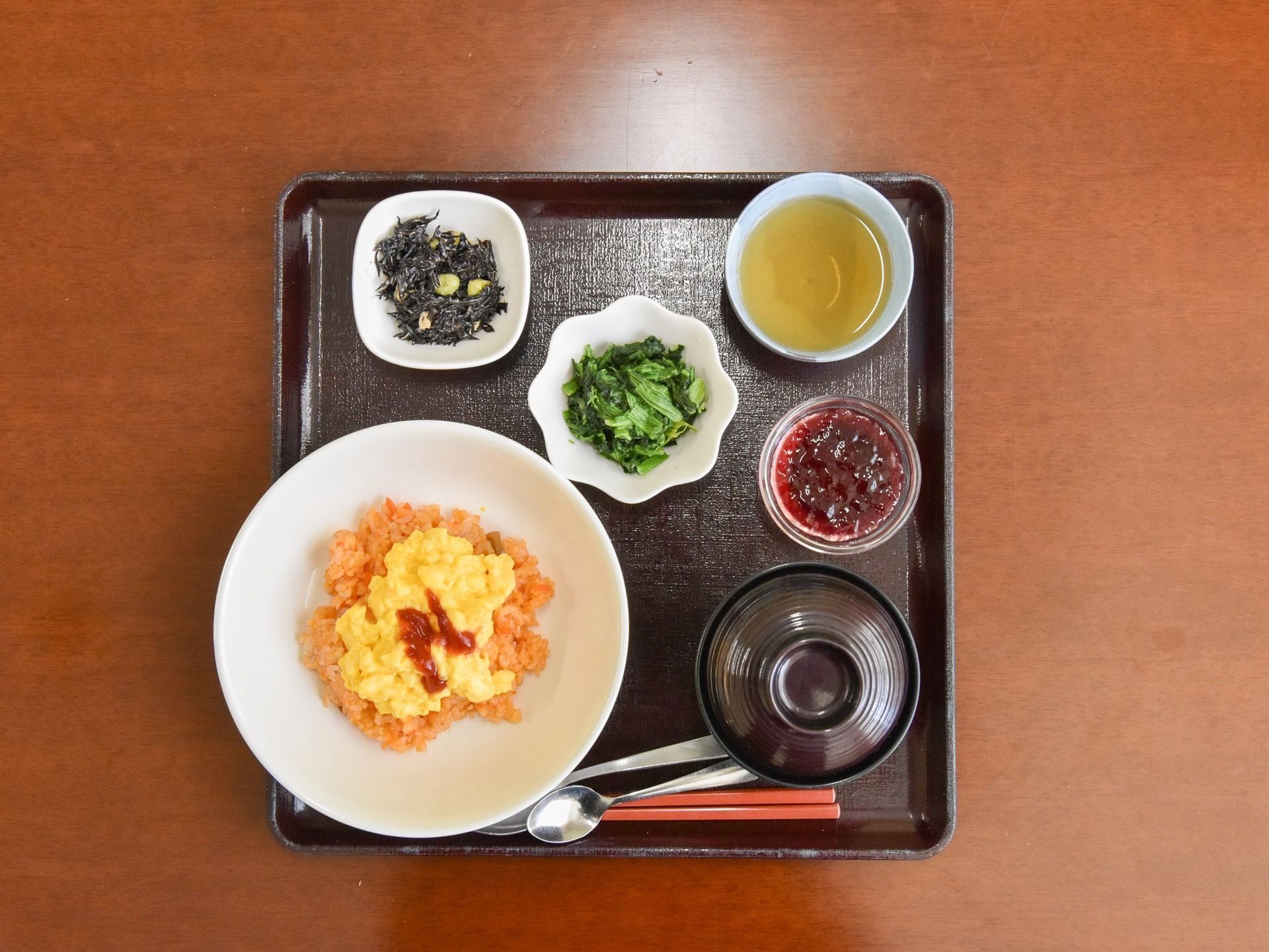 黒いトレーには、5つの器に食事が盛りつけられている。オムライスや和え物、ひじきの煮物など、栄養バランスの取れたメニューとなっている。
