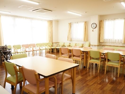 ライトグリーンの椅子がセットされた木製のテーブルセットが複数置かれた食堂の壁には時計が飾られている。
