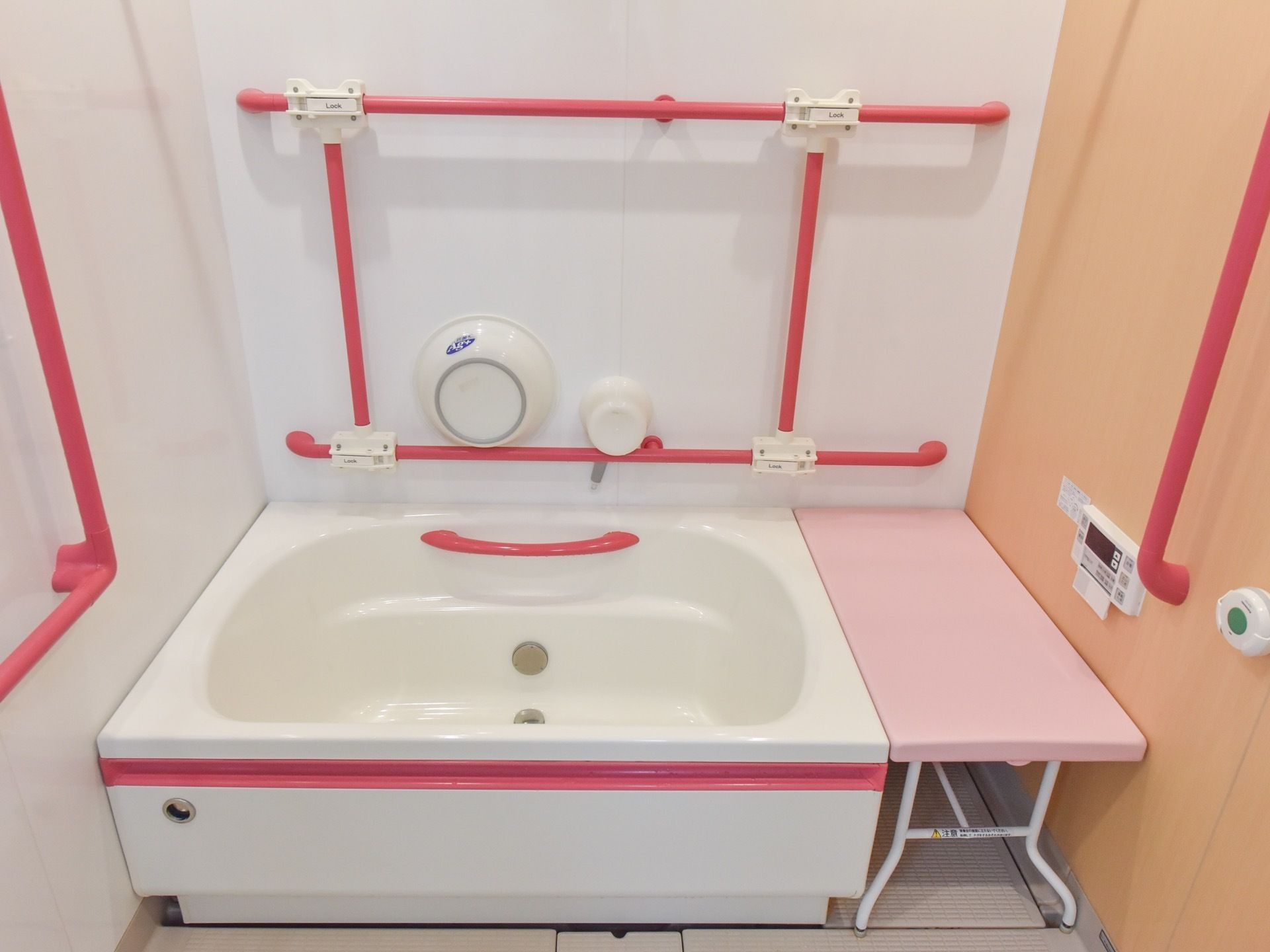 白を基調としたユニットバスタイプの浴室である。それぞれの壁にピンク色の手すりが設置されている。壁に洗面器と手桶が掛けられている。