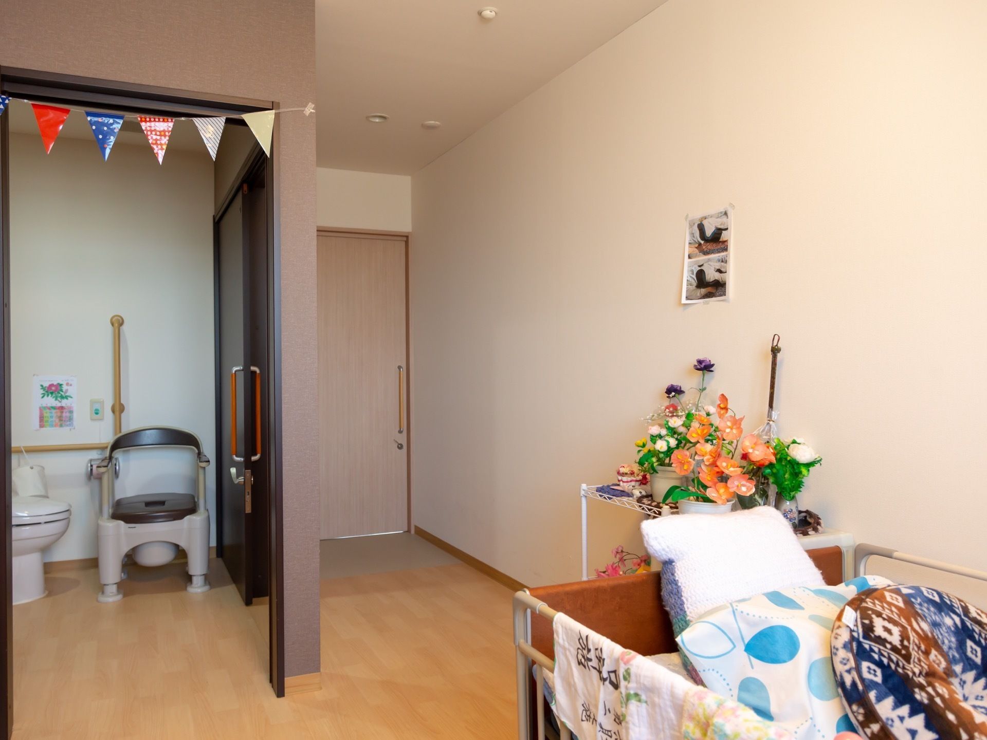 居室のドアはスライド式である。壁際にはベッドが設置されている。部屋の中にトイレがあり、便座の周りには手すりがついている。