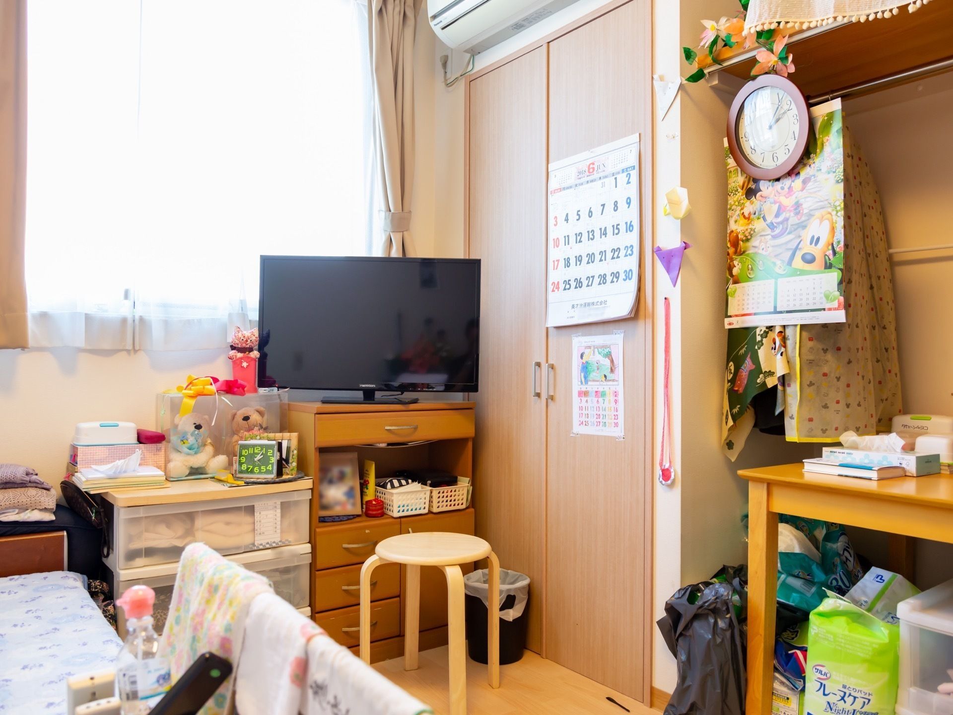 ベッドの周りのタンスや机の上に日用生活品が揃っている、生活感のある居室