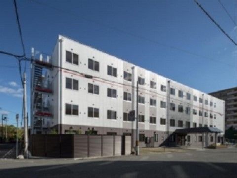 道路に面して建っている４階建ての建物で、一階の壁は茶色、二階以上は白い。玄関上には大きなひさしがある。