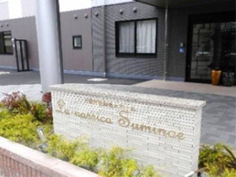 敷地入り口には植栽があり、施設名が書かれた看板がある。玄関扉はガラス製で、前はタイル貼りになっている。