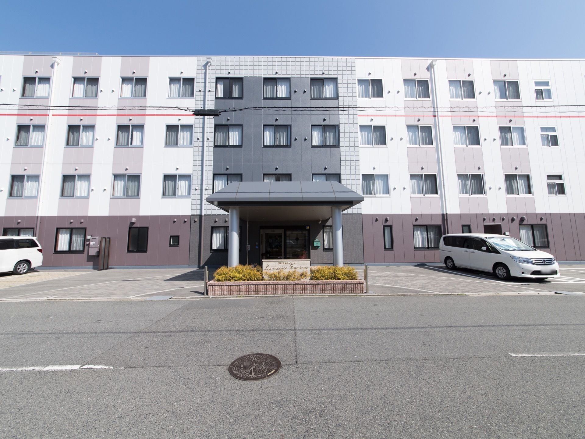 4階建ての施設は1階はブラウン、2階から上はベージュに塗り分けられている。玄関の上はアクセントでタイル張りになっている。