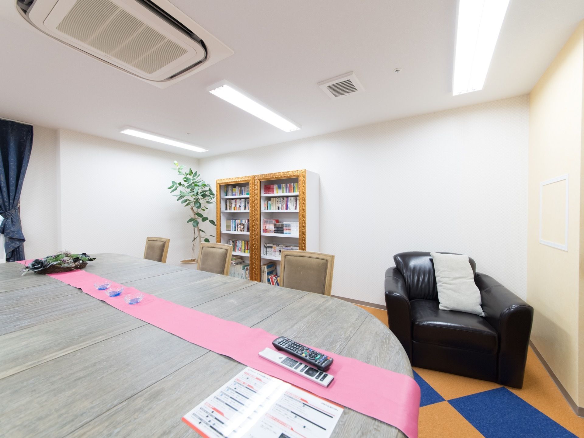 楕円の大きなテーブルと椅子が設置された部屋。奥には本棚があり、1人がけの黒いソファが置かれている。床は絨毯が敷かれている。