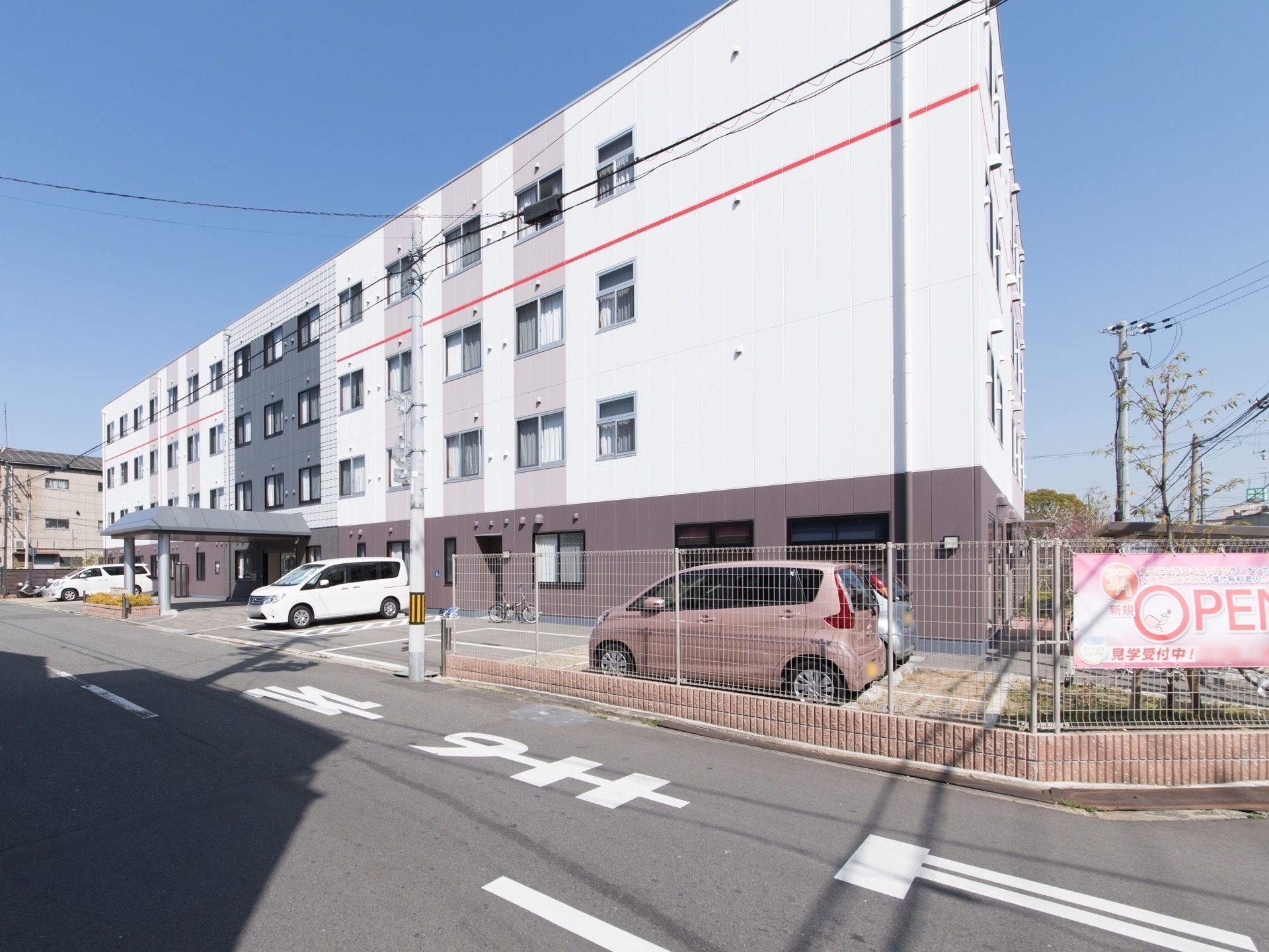 施設の正面右側からの外観。玄関の左右に駐車場が設けられている。施設周辺は視界を遮らないデザインのフェンスで囲まれている。