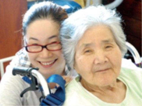 車椅子に乗りほほ笑む入居者様と、その後ろに座る笑顔の女性