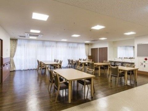 明るく開放的な空間にレースのカーテンや木の色合いの家具を配置している。入居者様にはお食事や各種イベントを楽しんでいただける。