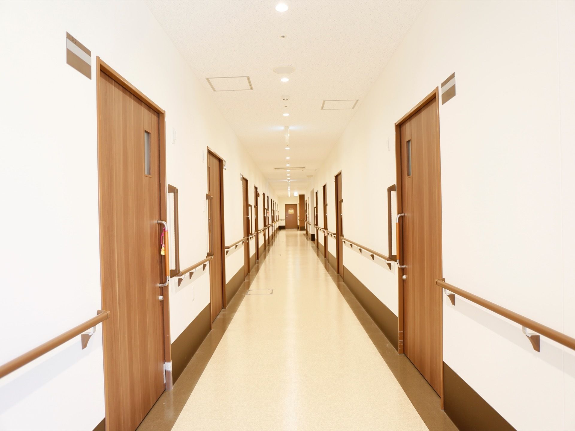廊下には居室のドアが並んでいる。スライドドアで、大きな取っ手が付いている。ドアの横の壁に、部屋番号のプレートが付いている。