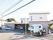 二階建ての住宅で、玄関前は駐車スペースが設けられている。植栽がされている道路側に、施設名の書かれた看板が立っている。