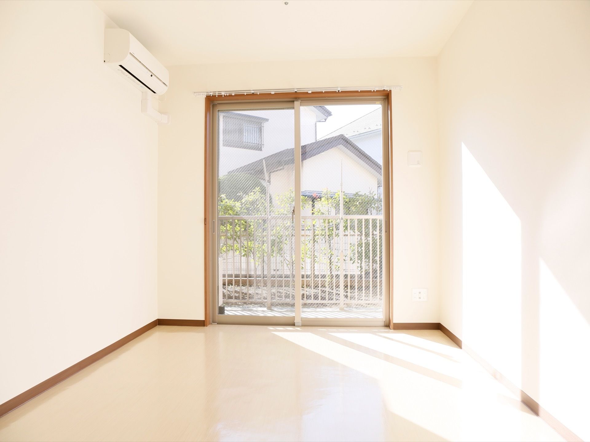 大きな掃き出し窓の向こうに、フェンスや植栽がされている。居室にはあらかじめエアコンが設置されている。