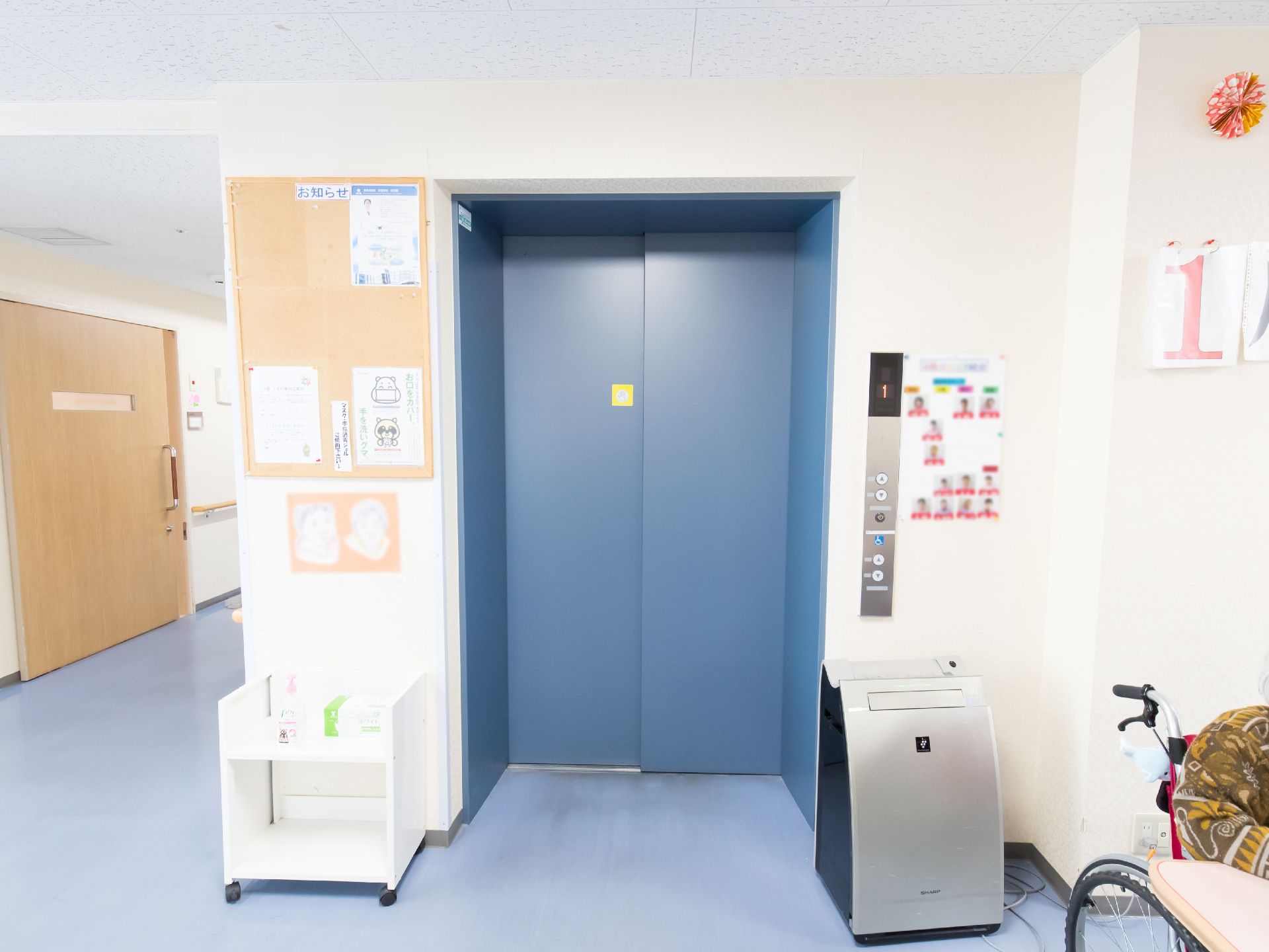 扉が青色のエレベーターが設置されている。扉の前には空気清浄機が置かれており、感染症の予防などに役立てられている。