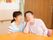 入居者様がリビングのテーブル席に座っている。横には、寄り添うように女性スタッフがしゃがんでいる。背後の壁には、手すりが設置されている。