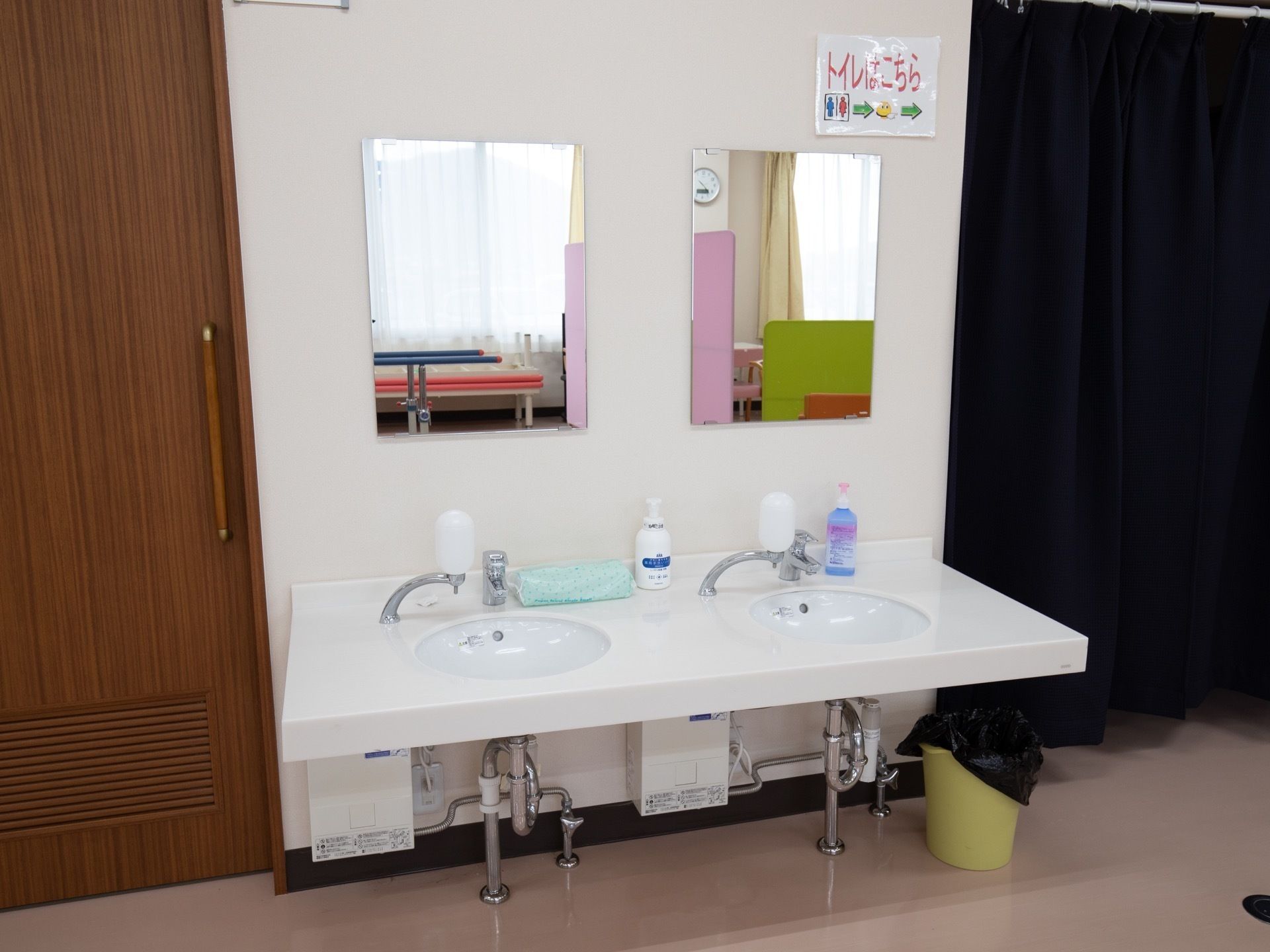 大きな鏡の付いた洗面台が２つ並んでいる。白で統一された清潔感があるデザインである。横にはゴミ箱が置かれている。