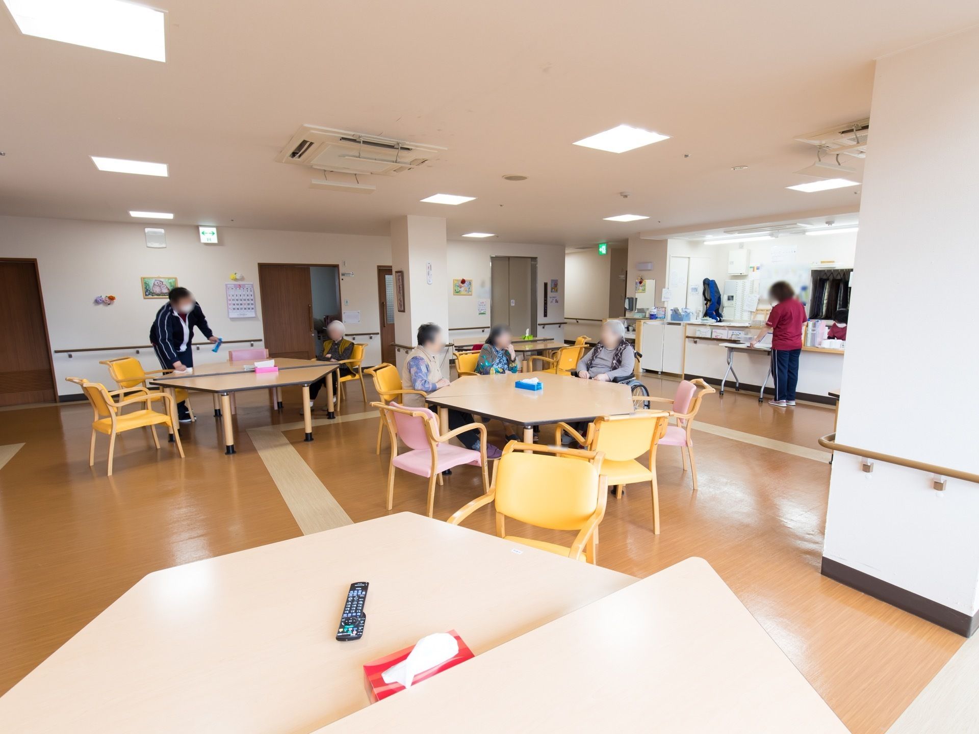 広々とした共有スペースである。入居者様が談話を楽しんでいる。スタッフが入居者様の様子を確認しながら、清掃を行っている。