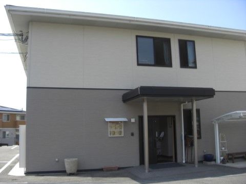 上下で外壁の色が異なり、庇のついた玄関がある二階建ての建物