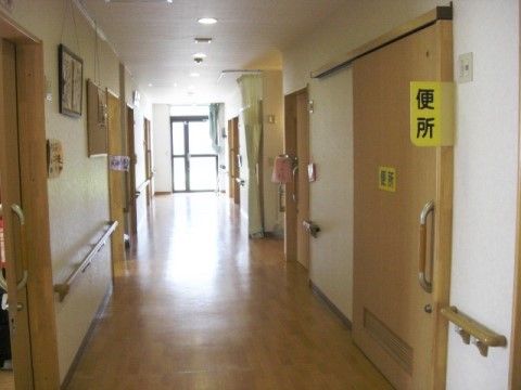 廊下は木目調の床となっており、右側にはトイレが設けられている。両サイドには、入居者様の居室が並んでいる。