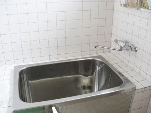 広々とした浴室の壁は全面白いタイル張りで、深さのあるステンレスの浴槽が設置されている。右側の壁には、水道がある。