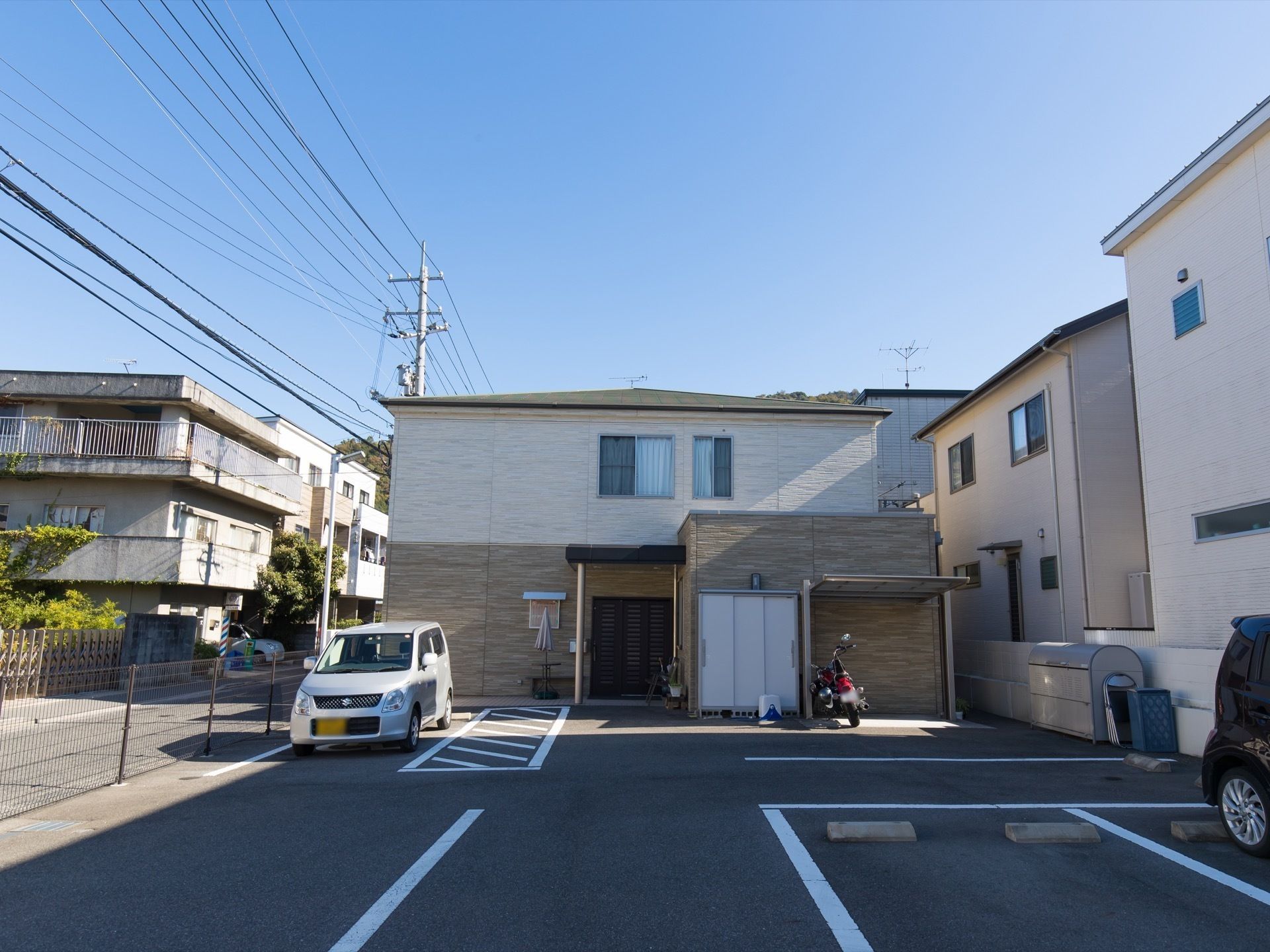 目の前に駐車場、駐輪場があり、物置が置いてある二階建ての建物