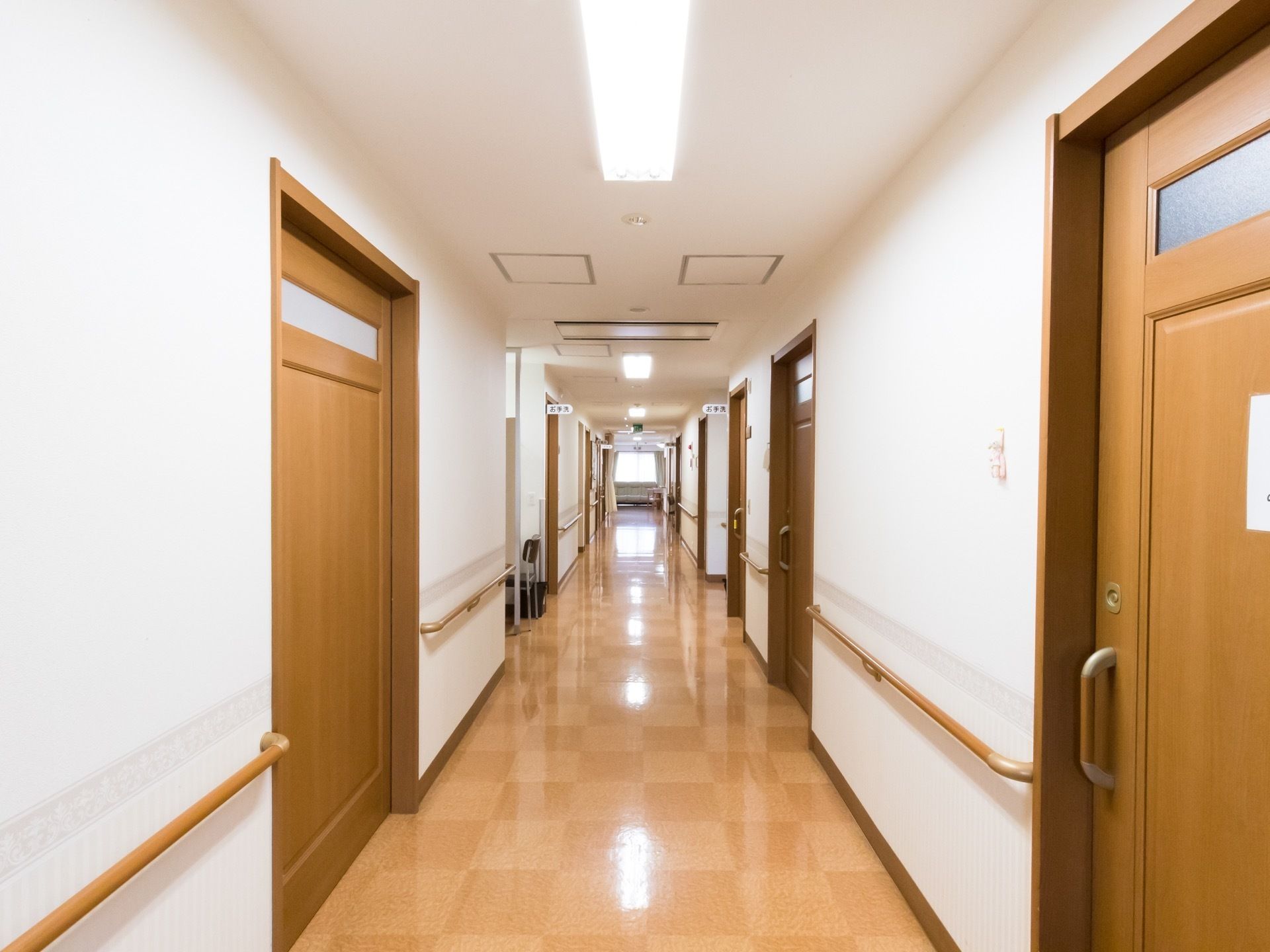 見通しが良く明るい廊下である。左右に並んでいる扉は引き戸になっている。転倒防止の手すりが壁に備わっている。