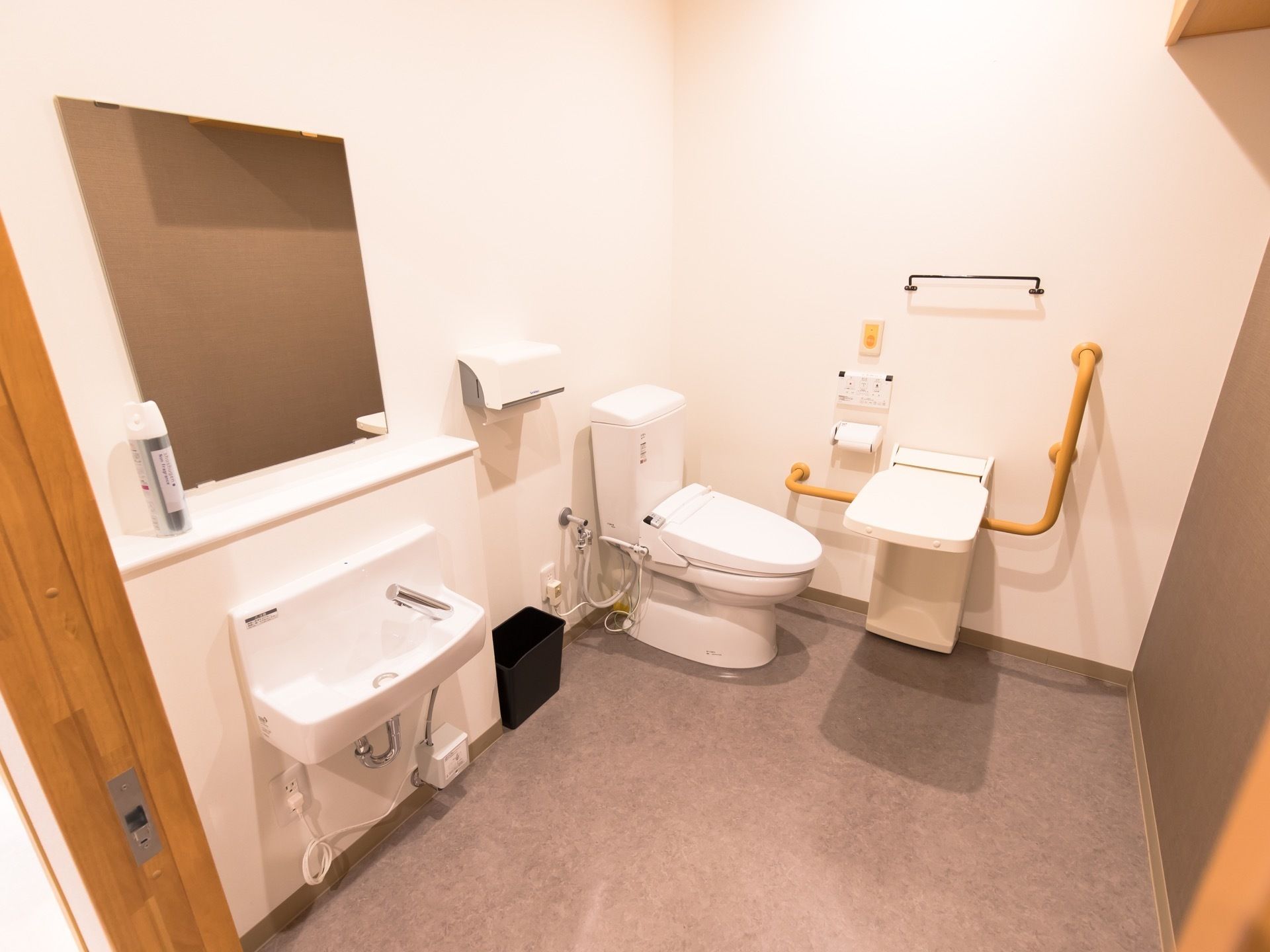 車椅子にも対応した広いトイレである。洗面台や温水洗浄便座が完備されており、壁に前傾姿勢保持用の手すりが設置されている。