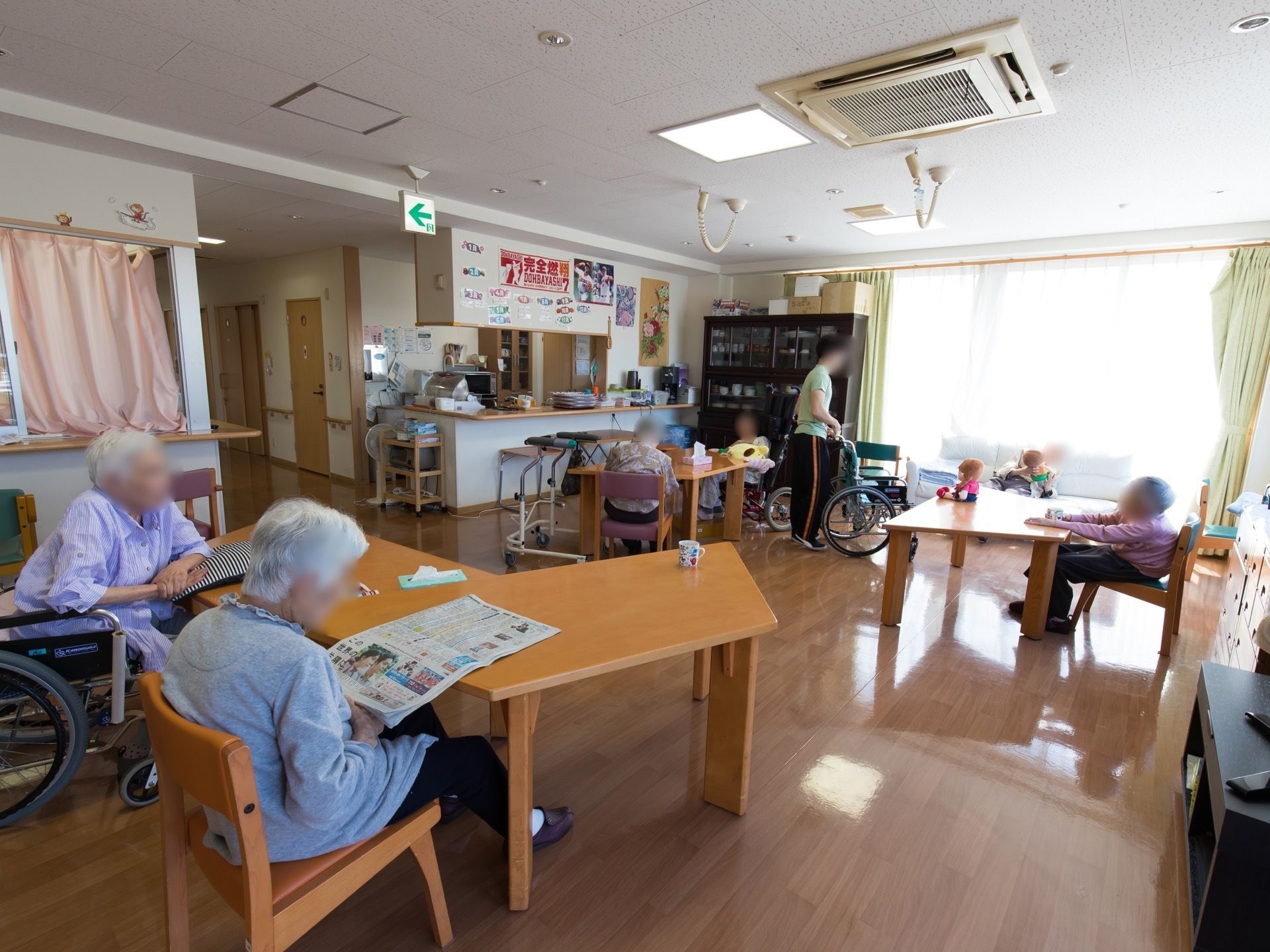 窓が大きく明るいリビングで、テーブルに向かい自由に過ごす入居者様