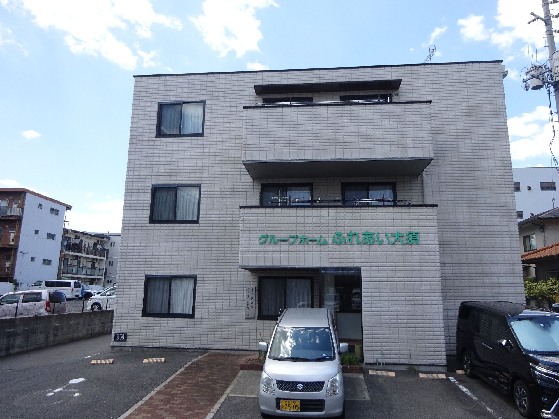 施設は、アパートのような外観の３階建ての建物である。２階と３階にベランダがついており、駐車場が建物前に設けられている。