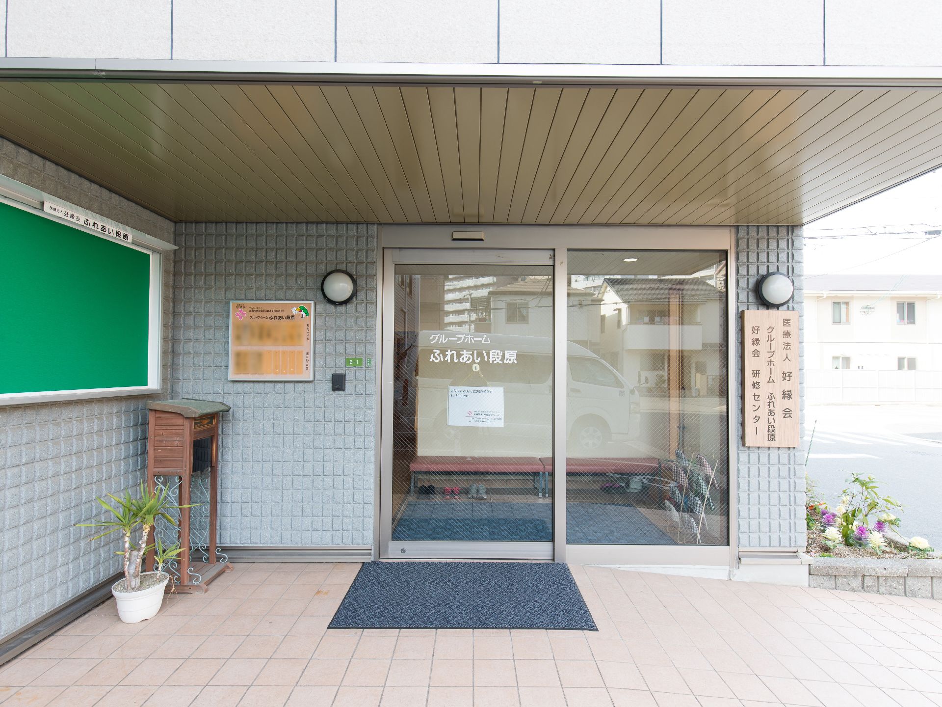 緑色の掲示板や花壇、観葉植物の置かれた自動ドアの玄関
